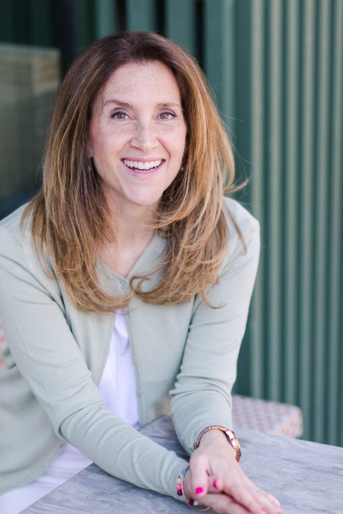 Sanna Koritz Smiling in Green Sweater Sitting at Outdoor Wooden Table